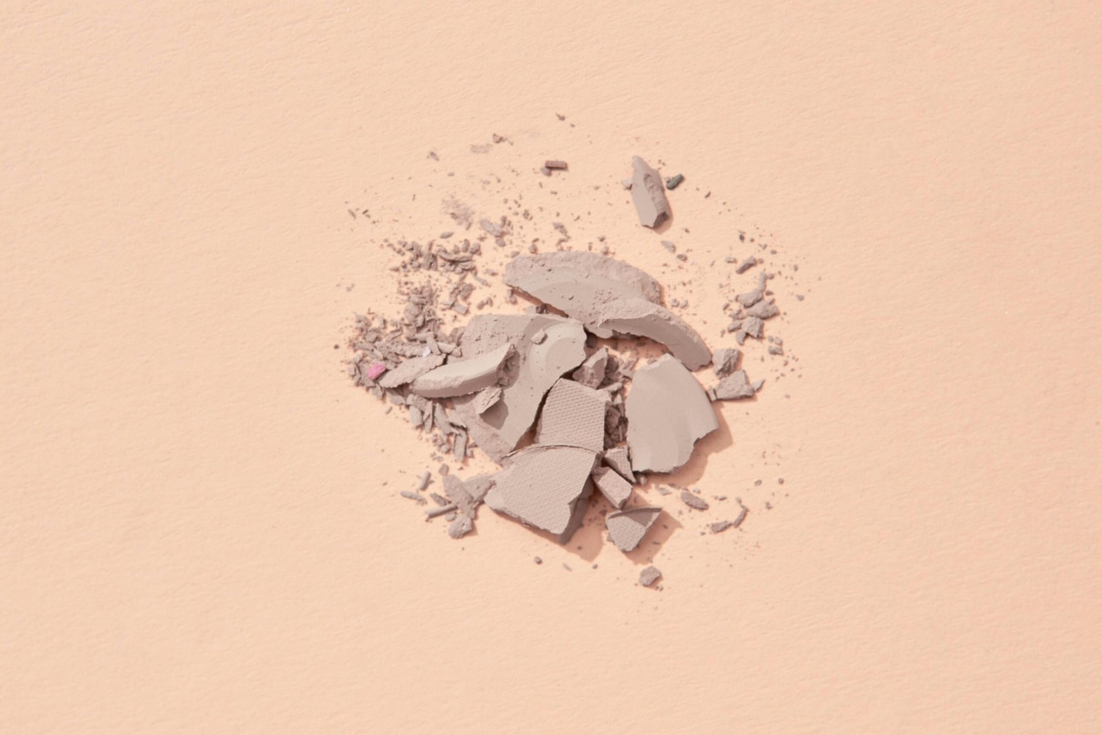 A close-up shot of crushed makeup powder on a beige background, showcasing texture and color contrast.